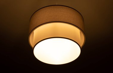 Bright lamp burning in a round lampshade, lampshade lighting indoors on a dark background
