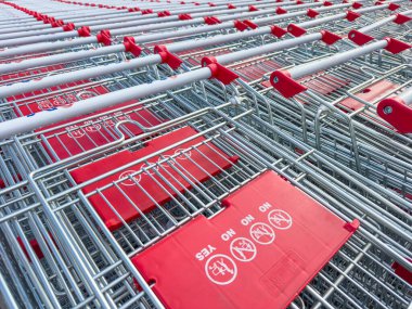 Large group of shopping cart trolley ready for consumers at supermarket. Rows of empty red and silver shopping carts. Retail, organization and consumer concept. Close up
