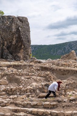 Amasya, Turkey - July 2022: Archaeologists working at ancient stone ruins with mountain, scenic cloudy sky background. People excavating rocky site. Ancient ruins dig area
