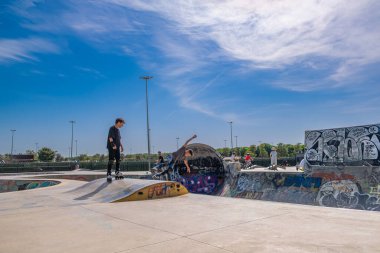 İstanbul, Türkiye - 17 Eylül 2022: Maltepe kentindeki kaykay parkında insanlar renkli grafiti ve mavi gökyüzü arka planıyla paten kayıyorlar. Güneşli yaz gününde kaykaycılar rampaya biniyor. Spor, kültür ve aksiyon konsepti