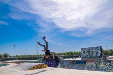 İstanbul, Türkiye - 17 Eylül 2022: Maltepe kentindeki kaykay parkında insanlar renkli grafiti ve mavi gökyüzü arka planıyla paten kayıyorlar. Güneşli yaz gününde kaykaycılar rampaya biniyor. Spor, kültür ve aksiyon konsepti