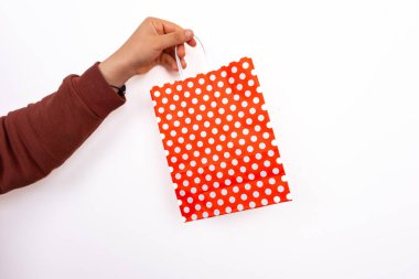 El ele tutuşan kırmızı benekli hediye paketi izole beyaz arka planda. Kırmızı noktalı alışveriş çantasını sürükleyen kişi. Hediye ve kutlama konsepti