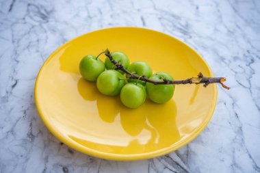 Fresh ripe green plums on yellow plate with branch on marble background surface