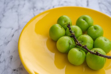 Fresh ripe green plums on yellow plate with branch on marble background surface