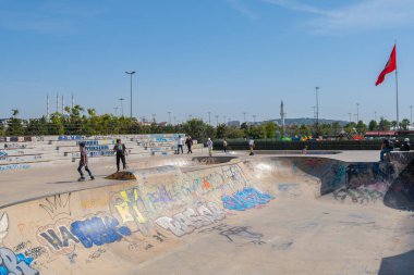 İstanbul, Türkiye - 17 Eylül 2022: Maltepe kentindeki kaykay parkında insanlar renkli grafiti ve mavi gökyüzü arka planıyla paten kayıyorlar. Güneşli yaz gününde kaykaycılar rampaya biniyor. Spor, kültür ve aksiyon konsepti