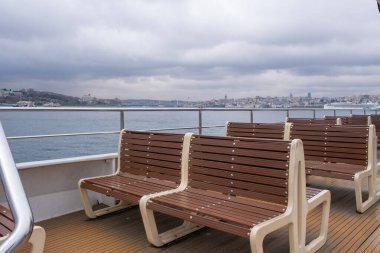 Wooden benches on the deck of a ferry boat with the city of Istanbul. Ferry boat sailing on the Bosphorus with the Istanbul skyline in the background. Cloudy day