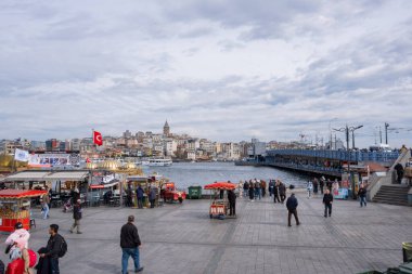 İstanbul, Türkiye - 10 Mart 2023: Eminonu Meydanı, İstanbul 'da yürüyen insanlar, ikonik Galata Köprüsü ve Altın Boynuz' un yer aldığı. Arka planda balık ve ekmek teknelerinden liman manzarası