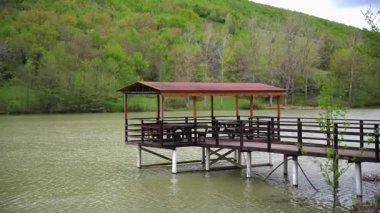 Tahta iskele ve sakin gölü kaplayan oturma alanı. Bereketli yeşil yamaç ormanı. Açık hava eğlence sahnesi