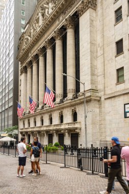New York 'ta tarihi bir bina, Amerikan bayraklarıyla süslenmiş, Wall Street' in finans bölgesi atmosferinin somut bir örneği. İnsanlar gelişigüzel ön planda toplanıp, şehir yaşamını ön plana çıkarıyorlar..