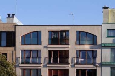 Modern bir apartmanda, çağdaş mimari tarzını sergileyen birden fazla büyük pencere ve balkon bulunur. Parlak, berrak gökyüzü şehir manzarasını güçlendiriyor..