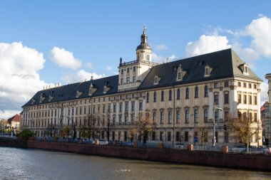 Polonya 'nın Wroclaw kentindeki nehir kıyısında büyük tarihi bir yapı bulunur. Güneşli hava mimarisinin detaylarını ortaya çıkarıyor ve mavi gökyüzü sahneyi büyütüyor..