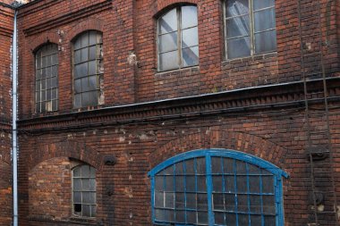 A weathered brick structure shows cracked walls and broken windows. Blue doors contrast with the old brick, revealing a scene of urban decay and neglect in daylight.