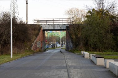 Sahne, sessiz bir yola yayılmış grafiti ile tuğladan bir köprü gösteriyor. Sabahın erken saatlerinde çevrede hafif bir parıltı oluşur. Bu da arka planda park halindeki arabaların olduğu yapraklı bir alanı ortaya çıkarır..