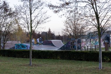 Kaykaycılar güneş batmaya başladığında bir kaykay parkında eğleniyorlar. Parlak renkli graffitiler rampaları süslerken ağaçlar bölgeyi çevreleyip doğanın bir dokunuşunu ekliyor..