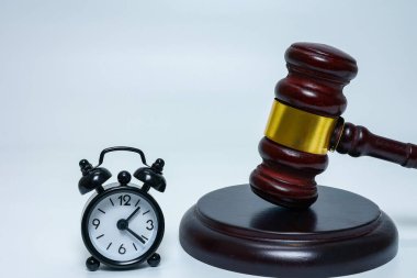 Beyaz zemin üzerinde siyah alarm saati ve ahşap tokmak Yasal Süre ve Mahkeme Uygulaması kavramını gösteriyor