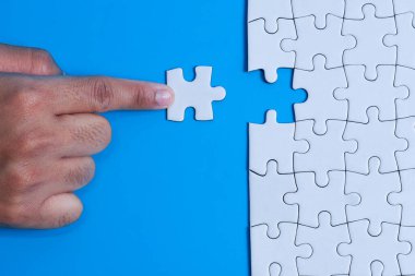 Mavi arka plandaki bulmacayı tamamlamak için boşluğa bir yapboz parçası yerleştirmek, entegrasyon veya iş birleşme kavramını gözler önüne sermek