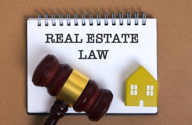 Gayrimenkul Hukuku metninin sarmal defteri, hakimler tarafından desteklenen tokmak ve ev modeli, mülkiyet düzenlemeleri, yasal otorite ve konut uyumunu sembolize eden.