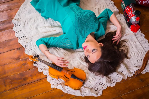 Belle femme brune couchée sur le sol parmi les décorations de nouvelles années en robe bleu vif, près du violon, photo d'en haut, pose plate Images De Stock Libres De Droits