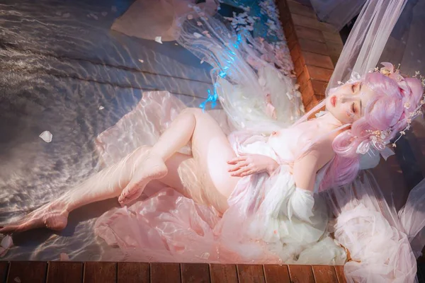 Pembe saçlı, dingin bir kadının, dalgalı kumaşlarla kaplandığı, büyüleyici, ruhani bir ruh hali yarattığı rüya gibi bir fanteziye dalmak..