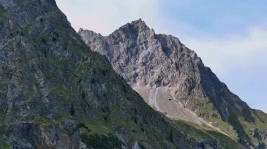 İsviçre Alpleri 'ndeki La Fouly çevresindeki görkemli kayalık tepelerin havadan ve yakından çekilmiş görüntüleri. Engebeli kayalıklar ve yeşil yamaçlar açık mavi gökyüzünün altında parlak yaz güneşiyle aydınlanır. Seyahat, macera ve doğa için mükemmel.