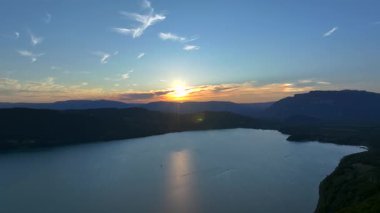 Etrafı dağlarla çevrili Lac du Bourget 'in günbatımı manzarası. Su açık bir akşam gökyüzünün altında turuncu ve mavi renklerde parlar.