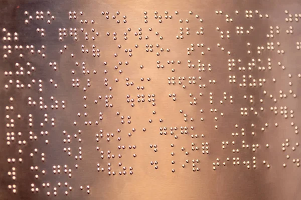 Yakından, desenli, metalik bir yüzey üzerindeki eğimli bir ışıkla aydınlatılmış altın kabartma alfabeyle yazılmış bir fotoğraf..