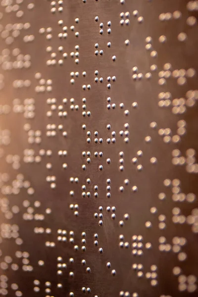 Yakından, desenli, metalik bir yüzey üzerindeki eğimli bir ışıkla aydınlatılmış altın kabartma alfabeyle yazılmış bir fotoğraf..