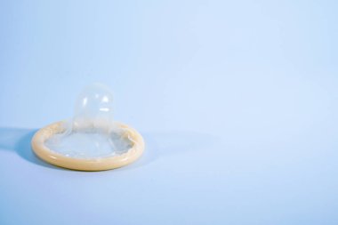 Mavi arka planda sarılmış bir prezervatif resmi. Prezervatif kullanmak bel soğukluğu, klamidya, trikomonez, hepatit B ve HIV riskini önemli ölçüde azaltır..