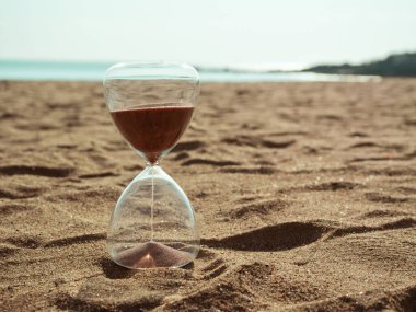 Temiz bir kum saati zamanı simgeler. Arkaplanda sonsuz okyanus ve ufuk olan kumsalda dinlenen güzel kumlar gibi..