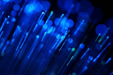 Karanlık bir zemin üzerinde dikey, yoğun mavi fiber optik ipliklerin soyut yakın çekimi, veri ve yüksek teknoloji bağlantısını öneriyor..