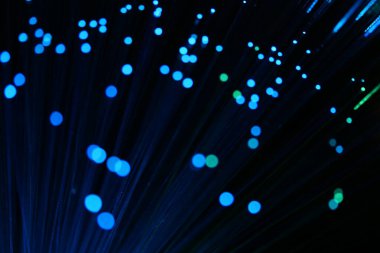 Karanlık bir zemin üzerinde dikey, yoğun mavi fiber optik ipliklerin soyut yakın çekimi, veri ve yüksek teknoloji bağlantısını öneriyor..