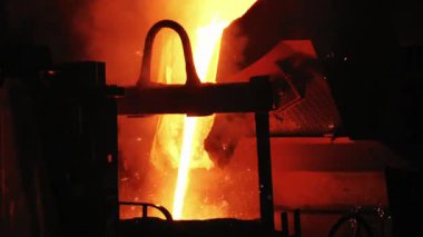 Büyük bir sanayi kepçesi, dökümhanenin döküm sürecinde önemli bir adımı vurgulayarak, daha küçük bir nakil kepçesine parlak bir erimiş demir akıntısı akıtıyor..