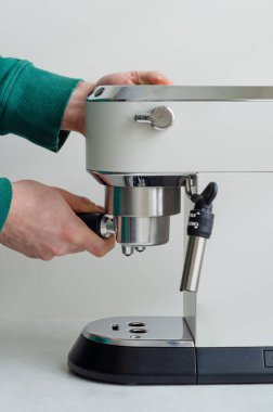 Erkeklerin elleri beyaz bir iskele filtresi kahve makinesine bir iskele filtresi sokuyor. Sıcak bir sabah kahvesinde evde espresso hazırlıyorum.
