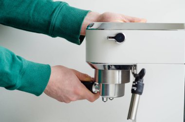 Erkeklerin elleri beyaz bir iskele filtresi kahve makinesine bir iskele filtresi sokuyor. Sıcak bir sabah kahvesinde evde espresso hazırlıyorum.