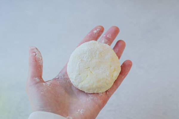 Close-up of a woman holding a freshly made cottage cheese pancake syrniki in her hand, ready for cooking or serving. Traditional Slavic cuisine. Cottage cheese baking recipes.