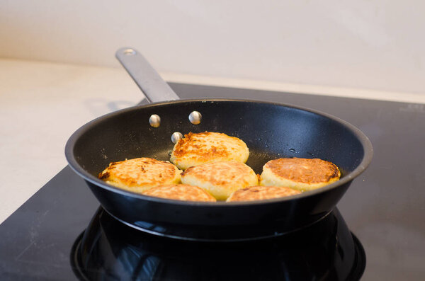 Freshly cooked golden cottage cheese pancakes syrniki on a frying pan. Traditional Slavic cuisine. Cottage cheese baking recipes. Perfect as a protein-rich breakfast 