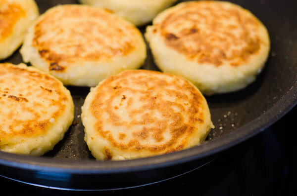 Freshly cooked golden cottage cheese pancakes syrniki on a frying pan. Traditional Slavic cuisine. Cottage cheese baking recipes. Perfect as a protein-rich breakfast 