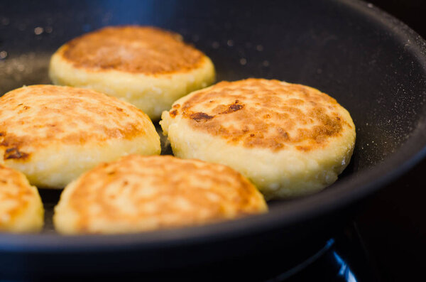 Freshly cooked golden cottage cheese pancakes syrniki on a frying pan. Traditional Slavic cuisine. Cottage cheese baking recipes. Perfect as a protein-rich breakfast 