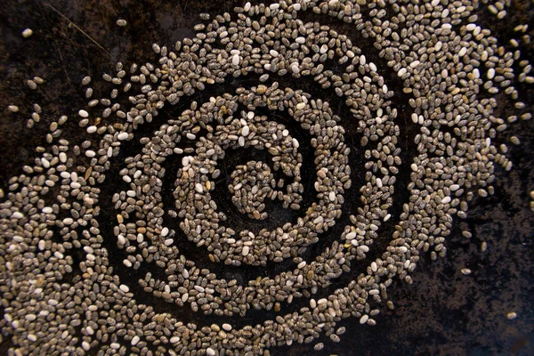 Siyah bir tava yüzeyinde chia tohumlarıyla çizilmiş spiral
