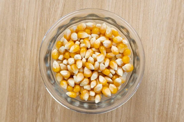 Açık renkli ahşap bir masada cam vazoda kurutulmuş mısır taneleri. Yakın ve üst görünüm.
