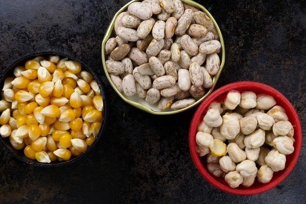 Mısır taneleri, fasulye ve nohut farklı yuvarlak kaplarda siyah bir tava yüzeyi üzerinde