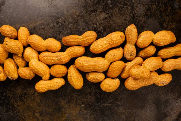 Kabuklu bir grup fıstık, siyah tava desenli arka planda yatay bir çizgide sıralanmış.