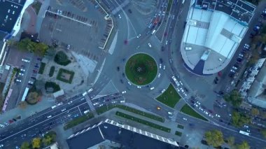 Akşam karanlığında kalabalık bir şehir kavşağının tepeden aşağı sinematik hava aracı görüntüsü. Farklı yönlere doğru sorunsuz giden arabalar kentsel altyapı ve modern ulaşımı gösteriyor. 