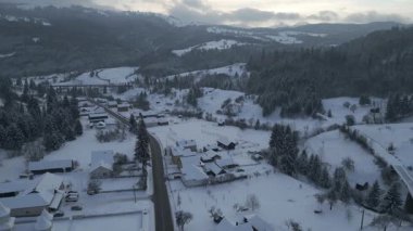 Drone 'un hava görüntüleri yavaşça yükseliyor ve karlı dağ köyünün üzerinde ilerliyor. Evleri, ormanlı tepeleri ve soğuk mevsimsel atmosferi olan kışın kırsal arazisi.
