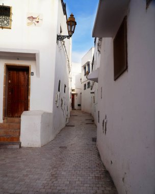 Beyaz binalarla kaplı açık renkli kaldırım taşlarından oluşan dar bir şerit. Bakış açısı mavi gökyüzü ve mimari unsurlar tarafından vurgulanmıştır..