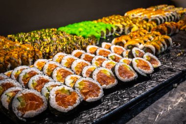 Taze balık, pirinç ve yosun da dahil olmak üzere suşi rulolarının lezzetli bir fotoğrafı bir tabakta servis ediliyor. Canlı renklerle güzel bir sunum, yemek, aşçılık ve restoran temaları için mükemmel..