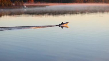 Sakin denizde gün doğumunda küçük bir teknede balık yakalayan balıkçı. Sis ve uzak orman kıyı şeridi ile çevrili. 4K ultra HD 'deki huzurlu doğa sahnesi..