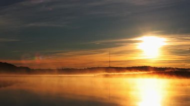 Güzel sonbahar gündoğumu deniz üzerinde altın güneş ışığı, yumuşak sis su ve orman kıyı şeridi üzerinde sürükleniyor, 4K ultra HD huzurlu doğa manzarası