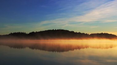 Güzel sonbahar gündoğumu deniz üzerinde altın güneş ışığı, yumuşak sis su ve orman kıyı şeridi üzerinde sürükleniyor, 4K ultra HD huzurlu doğa manzarası