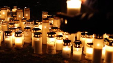 Sessiz bir mezarlıktaki mezara yanan bir mum koyan, mezar taşını aydınlatan yumuşak, ılık bir ışık ve 4K ultra HD 'de yakalanan bir anı ve yas anı yaratan kişi..